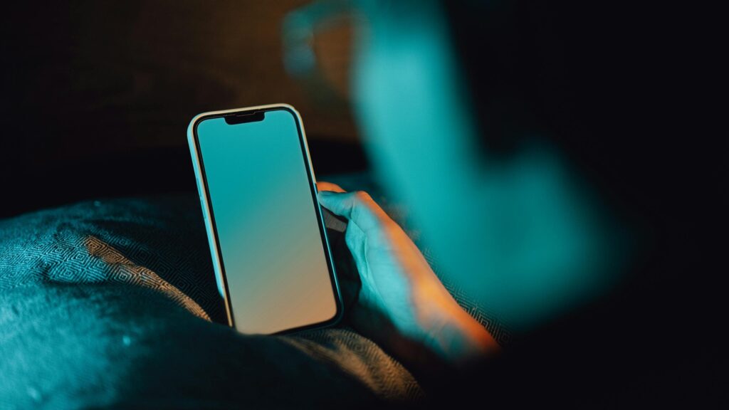 A man holding a smartphone searching for porn in a dark room.